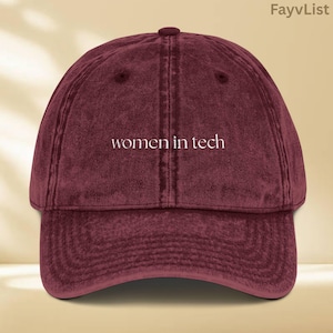 May include: A maroon vintage-style baseball cap with the text "women in tech" embroidered in white on the front.