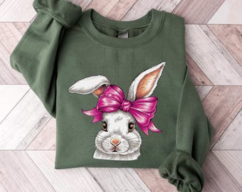 May include: A green sweatshirt with a white bunny rabbit wearing a pink bow. The bunny is looking at the viewer.