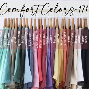 May include: A rack of 20 t-shirts in various colors, including Chalky Mint, Island Reef, Seafoam, Bay, Khaki, Light Green, Moss, Chambray, Blue Jean, Blossom, Crunchberry, Watermelon, Crimson, Orchid, Violet, Berry, Banana, Mustard, Terracotta, Yam, Espresso, Ivory, White, Pepper, and Black. The t-shirts are labeled with their color names.