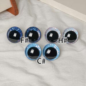 Pu&ograve; includere: Una collezione di cinque occhi rotondi per l'artigianato, con pupille nere lucide e bordi glitterati. I bordi sono in tonalit&agrave; di blu, rosa e bianco. Ogni occhio &egrave; etichettato con una combinazione di lettera e numero, come "F#" e "C#".