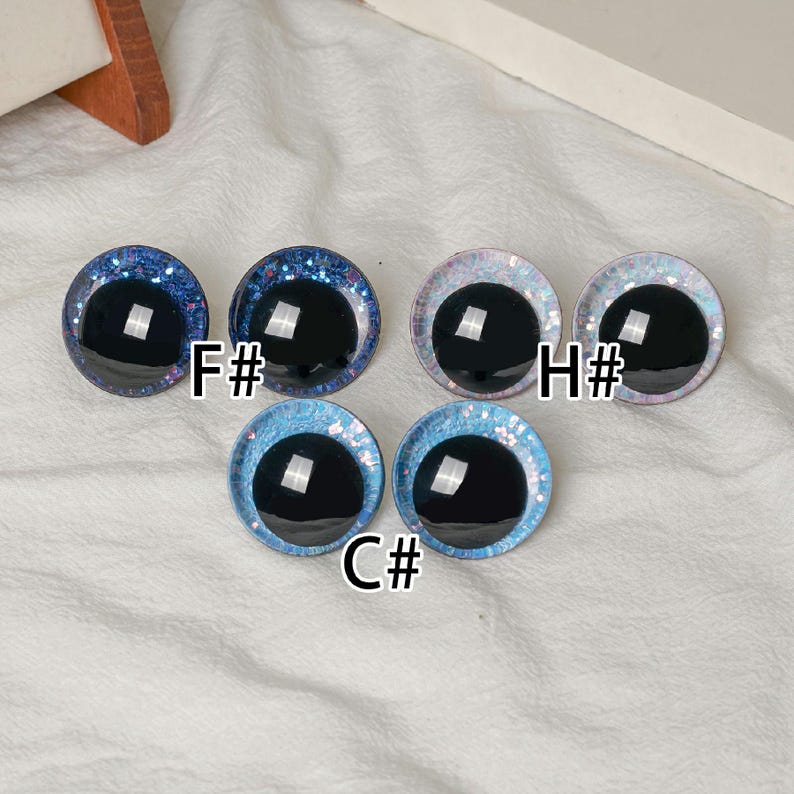 Pu&ograve; includere: Una collezione di cinque occhi rotondi per l'artigianato, con pupille nere lucide e bordi glitterati. I bordi sono in tonalit&agrave; di blu, rosa e bianco. Ogni occhio &egrave; etichettato con una combinazione di lettera e numero, come "F#" e "C#".