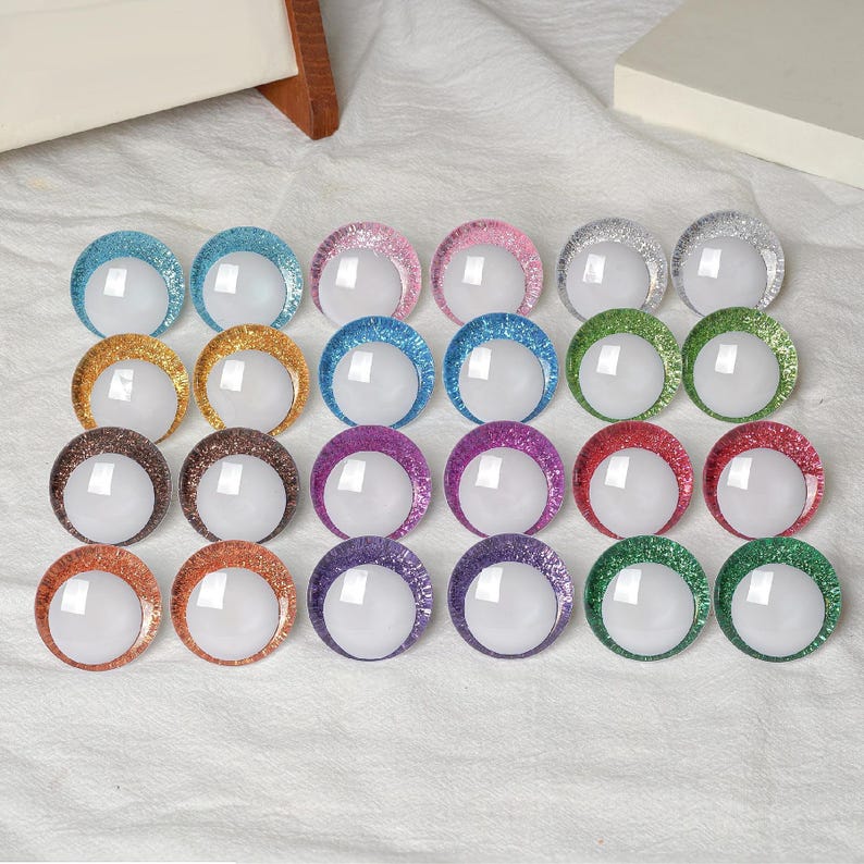May include: A collection of colorful, glitter-rimmed, round craft embellishments. The assortment includes various colors such as blue, pink, silver, gold, brown, purple, red, orange, and green. Each embellishment has a white, circular center.