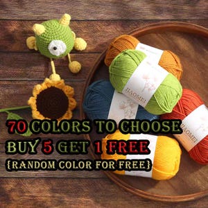 May include: An assortment of colorful yarn skeins and handmade crochet items, including a green monster and a sunflower. The image features text that reads "70 COLORS TO CHOOSE" and "BUY 5 GET 1 FREE". The yarn is in a wooden tray.