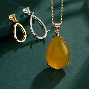 May include: A gold chain necklace with a teardrop-shaped pendant. The pendant is made of clear yellow glass and is set in a gold frame. Two smaller teardrop-shaped frames are also shown, one silver and one gold.