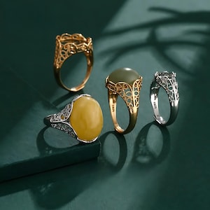 Puede incluir: Cuatro anillos con piedras de diferentes colores. Los anillos están hechos de plata y oro y tienen diseños intrincados. Las piedras son verdes, amarillas y transparentes.