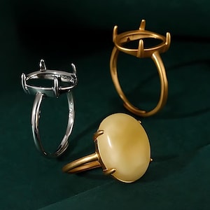 Peut inclure: Trois bagues sont présentées sur un fond vert foncé. Une bague est argentée avec un sertissage, une autre est dorée avec un sertissage, et la troisième est dorée avec une pierre ovale jaune clair. Les bagues sont conçues pour la fabrication de bijoux.