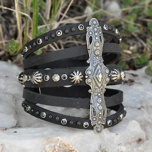 May include: A black leather wrap bracelet with a silver cross charm and black rhinestones.