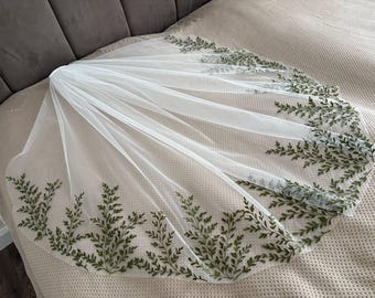 May include: A white bridal veil featuring an embroidered fern leaf pattern in green along the borders. The veil is crafted from a sheer, lightweight material, offering a soft and elegant appearance. Ideal for weddings or special events.
