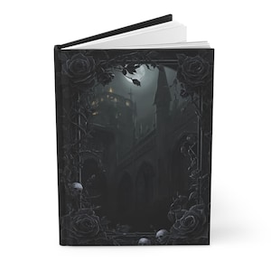 May include: Hardcover journal with a gothic-themed cover. The cover features a dark illustration of a castle under a full moon, framed by black roses, vines, and skulls. The journal is open, revealing white pages.