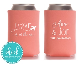 May include: Coral-colored can coolers with white text. One cooler reads "LOVE is in the air" with a heart and airplane graphic. The other says "Ava & JOE THE BAHAMAS". A teal logo is at the bottom.