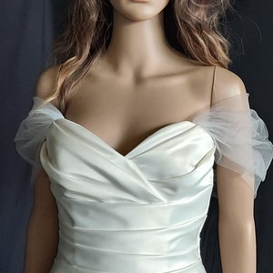 Puede incluir: Un vestido de novia blanco de hombros descubiertos con un corpiño ajustado y una falda fluida. El vestido tiene un diseño simple y elegante.