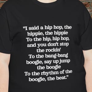 Peut inclure: T-shirt noir avec texte blanc. Le texte dit : "I said a hip hop, the hippie, the hippie, To the hip, hip hop, and you don't stop the rockin', To the bang-bang boogie, say up jump the boogie, To the rhythm of the boogie, the beat."