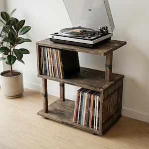 May include: A dark brown wooden record player stand with two open shelves for vinyl storage. The top shelf holds a silver and black turntable with a clear lid. The shelves are filled with rows of colorful vinyl records standing upright.