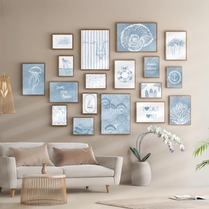 Pode incluir: Uma galeria de impress&otilde;es art&iacute;sticas emolduradas com tema costeiro. As impress&otilde;es apresentam ilustra&ccedil;&otilde;es em aquarela de conchas, elementos n&aacute;uticos e cenas de praia em tons de azul e branco. A arte de parede &eacute; exibida acima de um sof&aacute; branco.