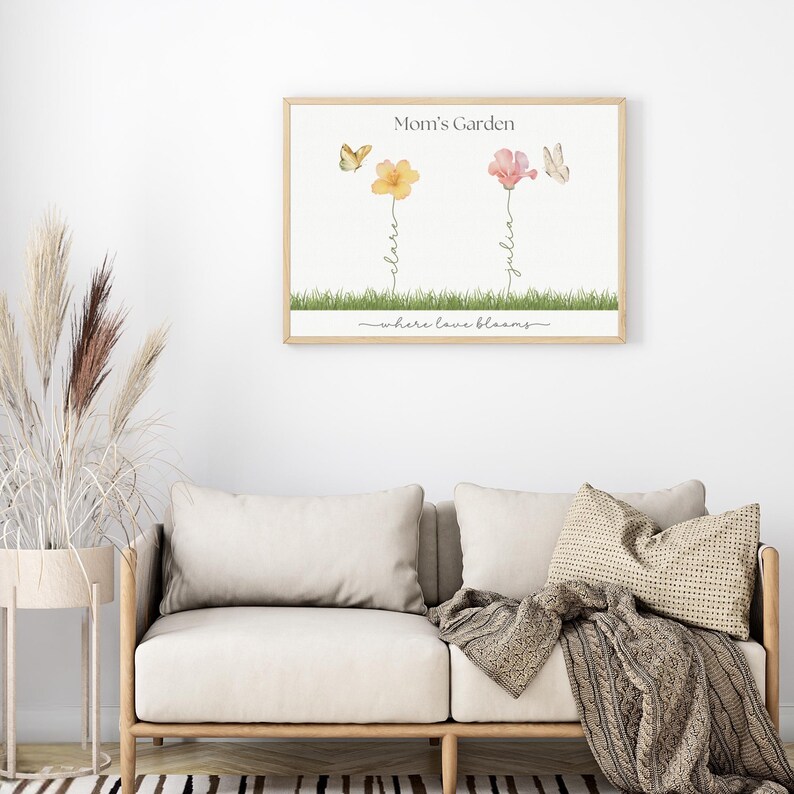 K&ouml;nnte beinhalten: Ein Aquarelldruck mit dem Text "Mom's Garden" und dem Satz "where love blooms". Der Druck zeigt zwei Blumen mit Schmetterlingen und die Namen "Claire" und "Julia", die auf den Stielen geschrieben sind.