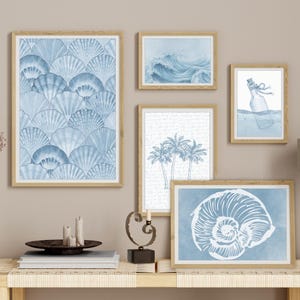 Pode incluir: Uma cole&ccedil;&atilde;o de impress&otilde;es de arte emolduradas com tema costeiro. As impress&otilde;es apresentam ilustra&ccedil;&otilde;es em aquarela de conchas, ondas do oceano, palmeiras e uma mensagem em uma garrafa, todas em tons de azul e branco. As molduras s&atilde;o castanho claro.