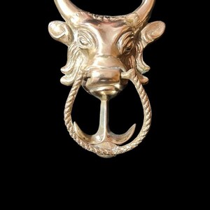 Puede incluir: Un llamador de puerta de cabeza de toro de oro con un diseño de cuerda y ancla.