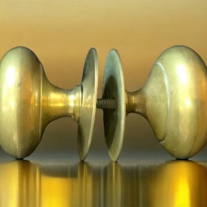 May include: A pair of antique brass door knobs with a decorative design. The knobs are connected by a metal plate.