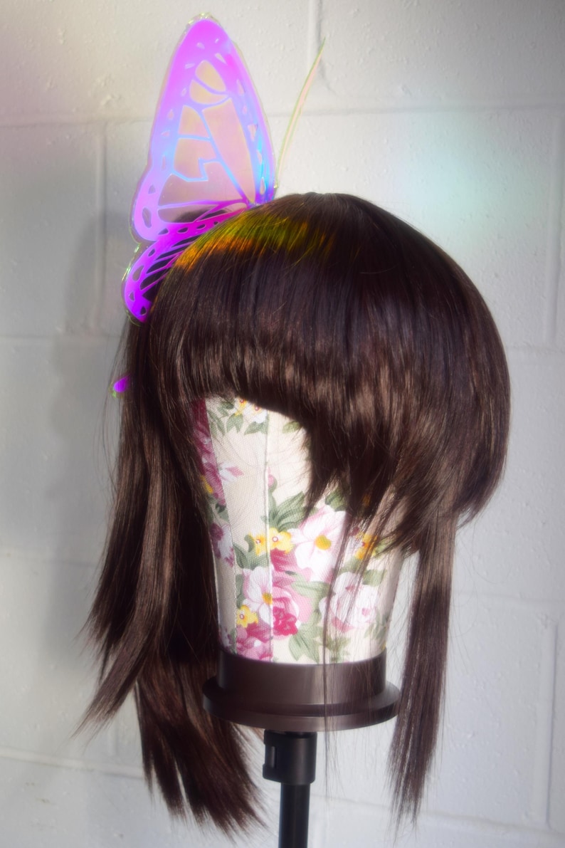 May include: A brown wig with a iridescent butterfly hair clip. The butterfly is purple, pink, and blue.