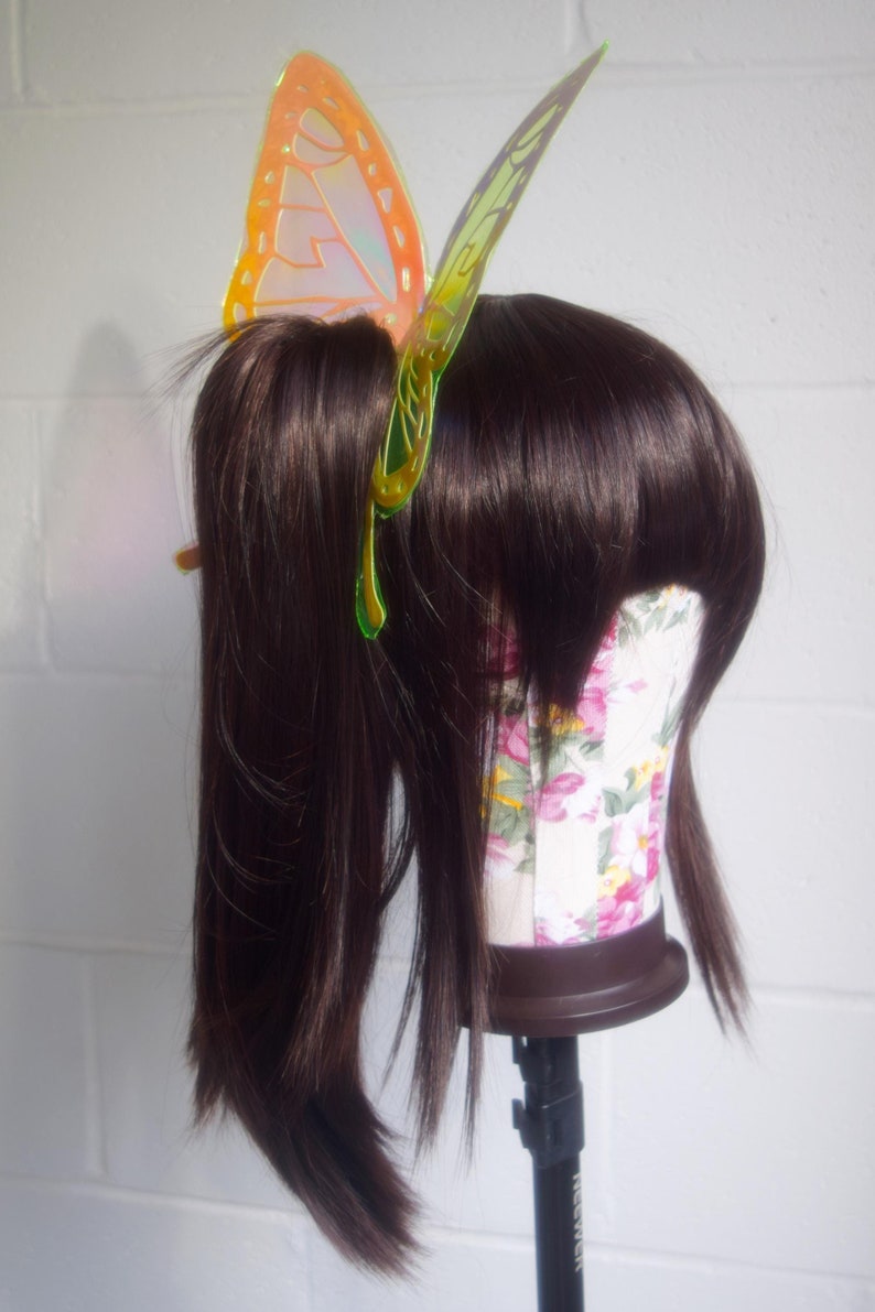 May include: A brown wig with a butterfly hair clip. The butterfly is iridescent and has a yellow, orange, and green color scheme.
