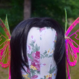 May include: A pair of iridescent butterfly wings with pink and green accents. The wings are made of a thin, translucent material and have a delicate, whimsical design.