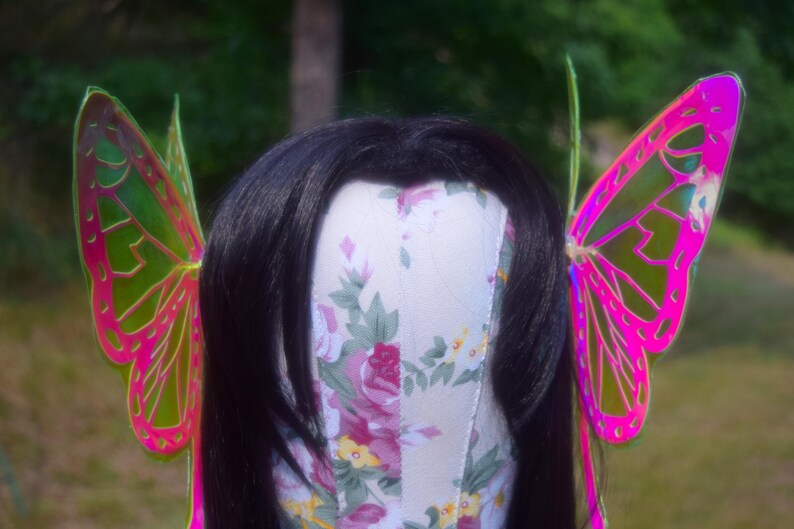 May include: A pair of iridescent butterfly wings with pink and green accents. The wings are made of a thin, translucent material and have a delicate, whimsical design.