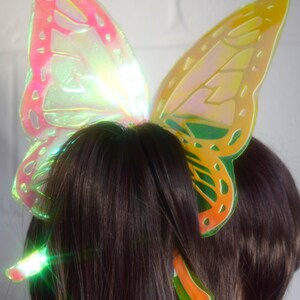 May include: A pair of iridescent butterfly hair clips in yellow, orange, green, and pink. The clips are made of plastic and have a shiny finish.
