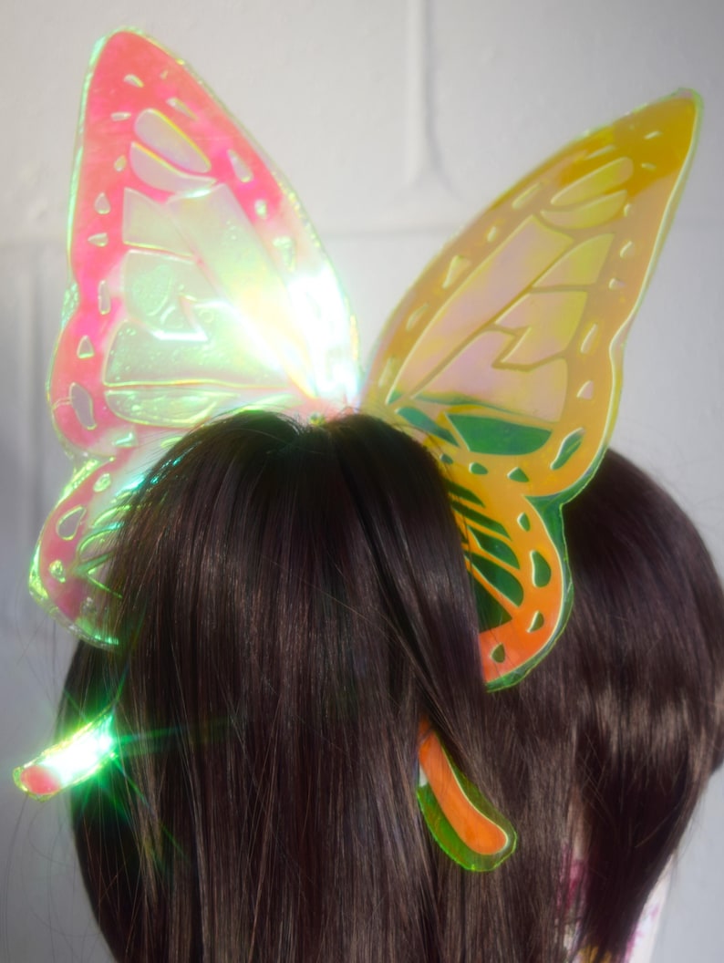 May include: A pair of iridescent butterfly hair clips in yellow, orange, green, and pink. The clips are made of plastic and have a shiny finish.