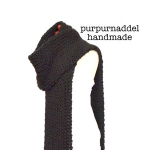 May include: A black knitted scarf with a hood, displayed on a mannequin. The scarf is long and rectangular, with a ribbed texture and a ruffled edge. The text "purpurnaddel handmade" is in the upper right corner.