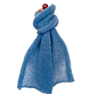 May include: A light blue knitted scarf, knotted at the top. The scarf is made of a soft, lightweight material. A small, round, dark red object is visible at the top of the knot. The scarf is displayed against a white background.
