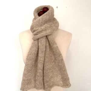 May include: A light brown knitted scarf with a fringed edge. The scarf is draped around a mannequin's neck.