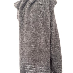 May include: A gray, oversized knitted shawl displayed on a mannequin. The shawl is made of a thick, textured yarn and features a draped design. The color is a muted gray, and the garment appears warm and cozy.