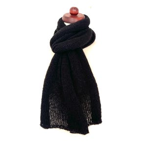 May include: A black knitted scarf draped over a wooden mannequin head. The scarf is made of a thick, textured yarn and has a simple, classic design. The scarf is a solid black color and appears to be warm and cozy.