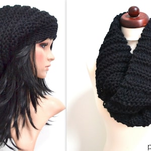 May include: A black knit beanie and a black infinity scarf. The beanie is oversized and slouchy. The infinity scarf is thick and chunky. The items are displayed on a mannequin head and neck. The text "designed by purpurnaddel" is visible.