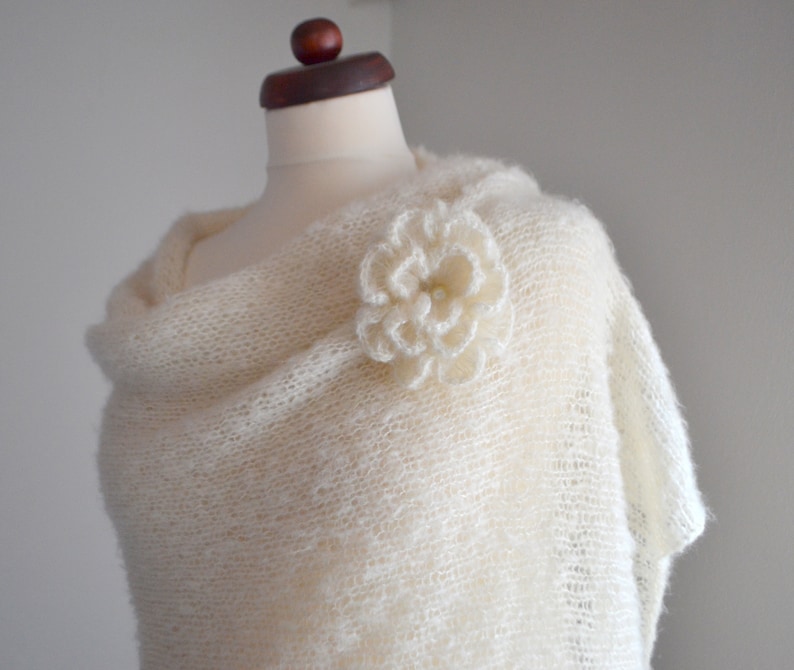May include: A white knitted shawl with a crocheted flower embellishment.