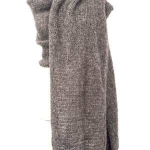 May include: A gray knitted scarf displayed on a mannequin. The scarf is a solid color, with a thick, textured knit. The scarf is long and drapes down the front of the mannequin. The scarf is made of a soft, warm material.