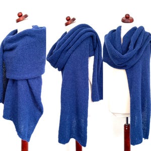 May include: A deep blue knitted scarf displayed on a mannequin. The scarf is thick and appears to be hand-knitted, with a textured appearance. The scarf is draped in multiple ways, showcasing its versatility and design.