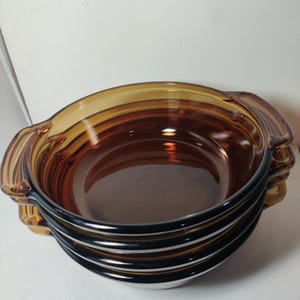 May include: A set of four amber glass baking dishes with handles. The dishes are stacked on top of each other.