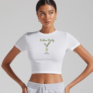 May include: White cropped t-shirt with short sleeves and the text "Extra Dirty" in green lettering. A green martini glass with olives is printed on the shirt.