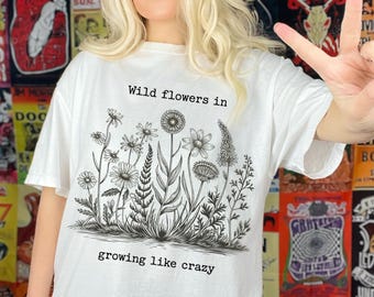 May include: White t-shirt with a black and white illustration of wildflowers and the text "Wild flowers in growing like crazy".