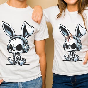 May include: Two white t-shirts with a cartoon image of a skeleton bunny wearing headphones. The bunny on the left has no bow, while the bunny on the right has a black and white polka dot bow.