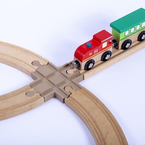 May include: A wooden toy train set with a red engine and a green passenger car on a wooden track. The train is on a brown wooden track with a tan intersection piece. The train has black wheels and is on a white background.