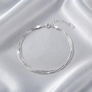 May include: A multi-strand silver bracelet featuring three thin, flexible snake chains that converge at a circular spring ring clasp, finished with a small dangling metal tag at the end of the adjustable extension chain.