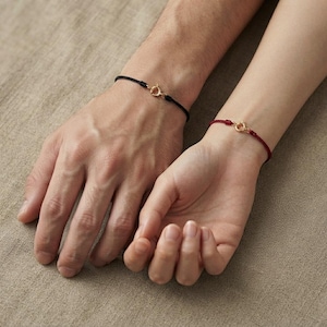 Peut inclure: Deux bracelets en cordon, l'un noir et l'autre rouge, chacun doté d'un fermoir à ressort circulaire doré. Ces bracelets sont des bandes fines et minimalistes conçues pour être portées au poignet, avec un mécanisme de fermeture métallique simple.