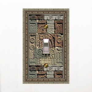 May include: Decorative light switch cover featuring a stone-like design with carved relief patterns. The cover has a rectangular shape with a central toggle switch and two brass-colored screws. The frame around the switch cover has a textured, stone-like appearance.