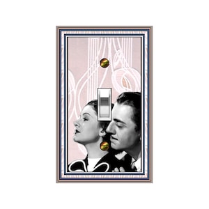 May include: A decorative light switch cover featuring a vintage black and white image of a man and woman. The cover has a pink background with a white art deco design, a white switch, and gold-colored screws. The frame has a navy blue and gold border.