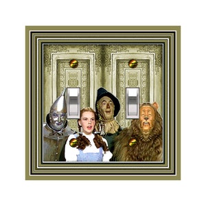 May include: A light switch plate featuring a vintage-style double door design with a scene from the Wizard of Oz. Dorothy, the Scarecrow, the Tin Man, and the Cowardly Lion are standing in front of the doors. The switch plate is framed in a gold-colored frame.