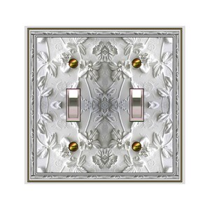 May include: White, floral-patterned double light switch cover with a decorative border. The cover features two silver toggle switches and brass-colored screws. The design includes raised floral and leaf details.