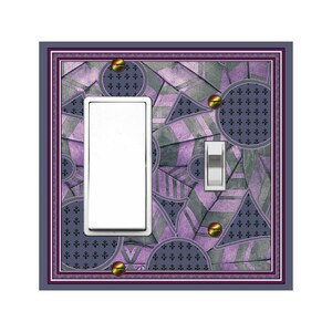 May include: A light switch cover with a geometric pattern in shades of purple and gray. The pattern includes circles, triangles, and lines. The switch cover has a white light switch and a white toggle switch.