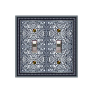 Puede incluir: Una placa de interruptor doble con un diseño decorativo plateado y azul. La placa tiene un patrón decorativo de remolinos ornamentados y una superficie texturizada.